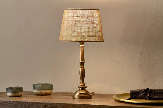 Elegant table lamp glowing softly on a wooden bedside table with a book beside it.